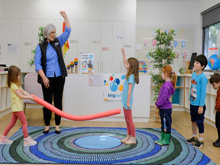 Kids playing a water safety game with a pool noodle